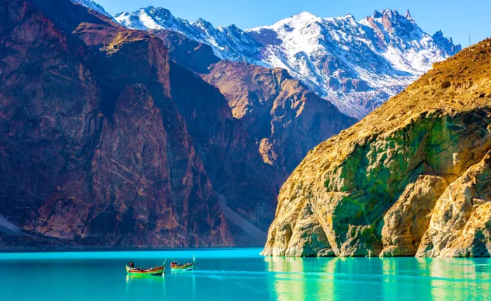 A serene view of Attabad Lake in Gilgit-Baltistan, Pakistan, with a boat gently gliding on its turquoise waters, surrounded by rugged mountains.