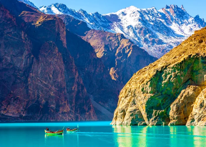 A serene view of Attabad Lake in Gilgit-Baltistan, Pakistan, with a boat gently gliding on its turquoise waters, surrounded by rugged mountains.