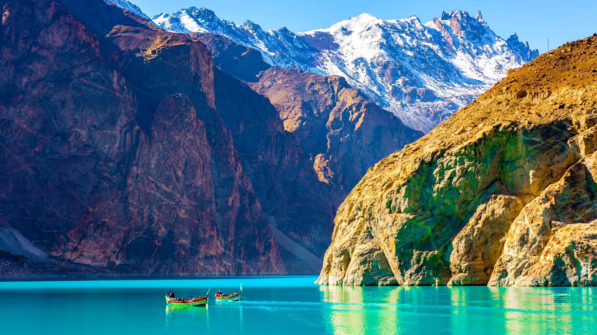 A serene view of Attabad Lake in Gilgit-Baltistan, Pakistan, with a boat gently gliding on its turquoise waters, surrounded by rugged mountains.