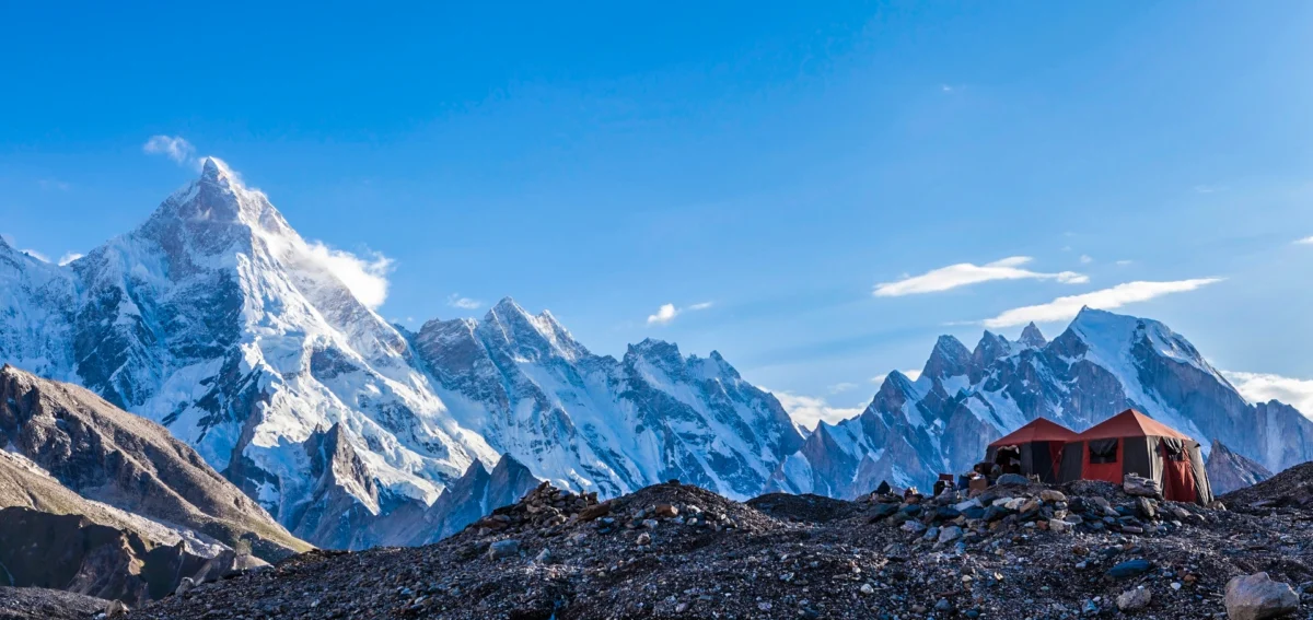 Scenic campsite nestled along the trail to Gondogoro la, part of the K2 and Gondogoro La Trek, surrounded by majestic mountains and lush greenery.